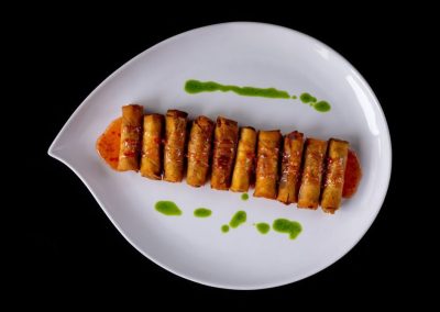 Delicious spring rolls served with sauce and green garnish on a white plate.