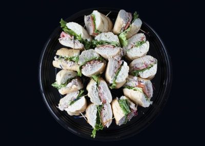 Assorted sandwich platter with bread, meats, cheese, and greens on black background.