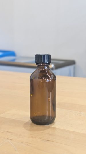 Small brown glass bottle with black plastic cap on wooden surface.