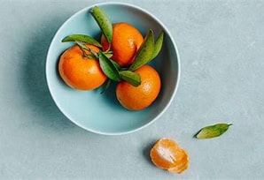 Fresh mandarin oranges with green leaves in a light blue bowl.