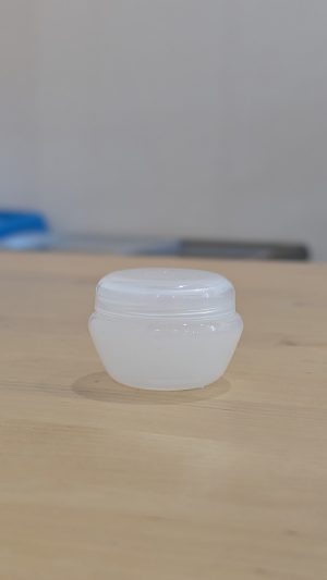Large white lip balm pot on wooden surface for skincare.