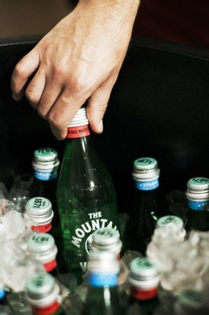 Hand opening Mountain Valley Spring Water bottle among other bottled waters.