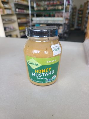 Organic honey mustard jar on store counter with store shelves in background.