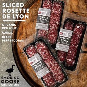Sliced Rosette De Lyon charcuterie on wooden board with packaging labels visible.