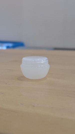 Small white lip balm container on a wooden surface.