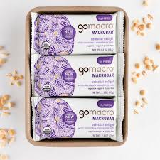 Three Go Macro White Chocolate Macadamia Nut bars in a box with scattered nuts.