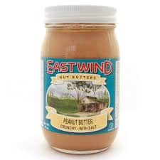 Jar of East Wind crunchy salted peanut butter with farm scene label.