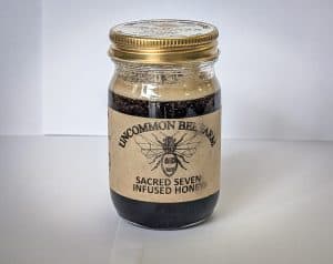 Jar of Sacred Seven Infused Honey with bee logo and gold lid.