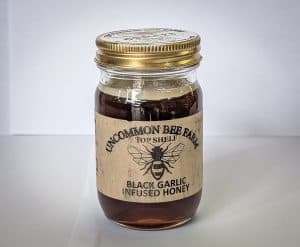 Jar of black garlic infused honey with Uncommon Bee label on white background.