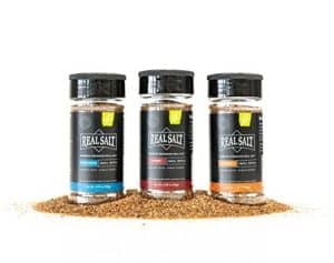 Three jars of Redmond Real Salt Smoked Juice with salt crystals and smoked salt in front.