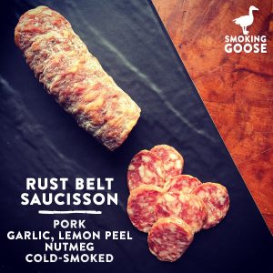 Rust Belt Saucisson pork sausage slices on black surface with Smoking Goose logo.
