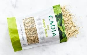 Cadia hemp seeds 12oz package with spilled seeds on white surface.