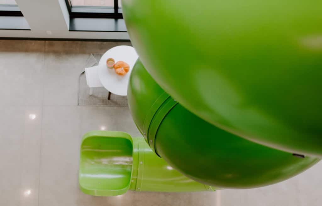 Bright green indoor playground slide with a small white table nearby.