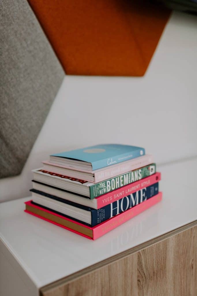 Stack of real estate books on a white nightstand in a modern home.