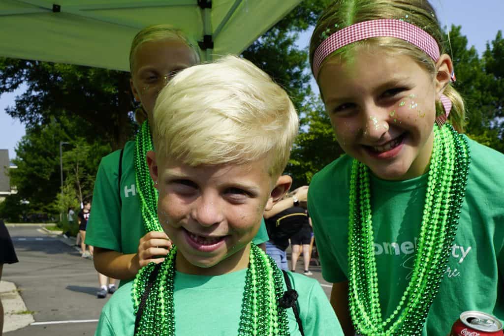 Kids smiling at community event wearing green beads and t-shirts.