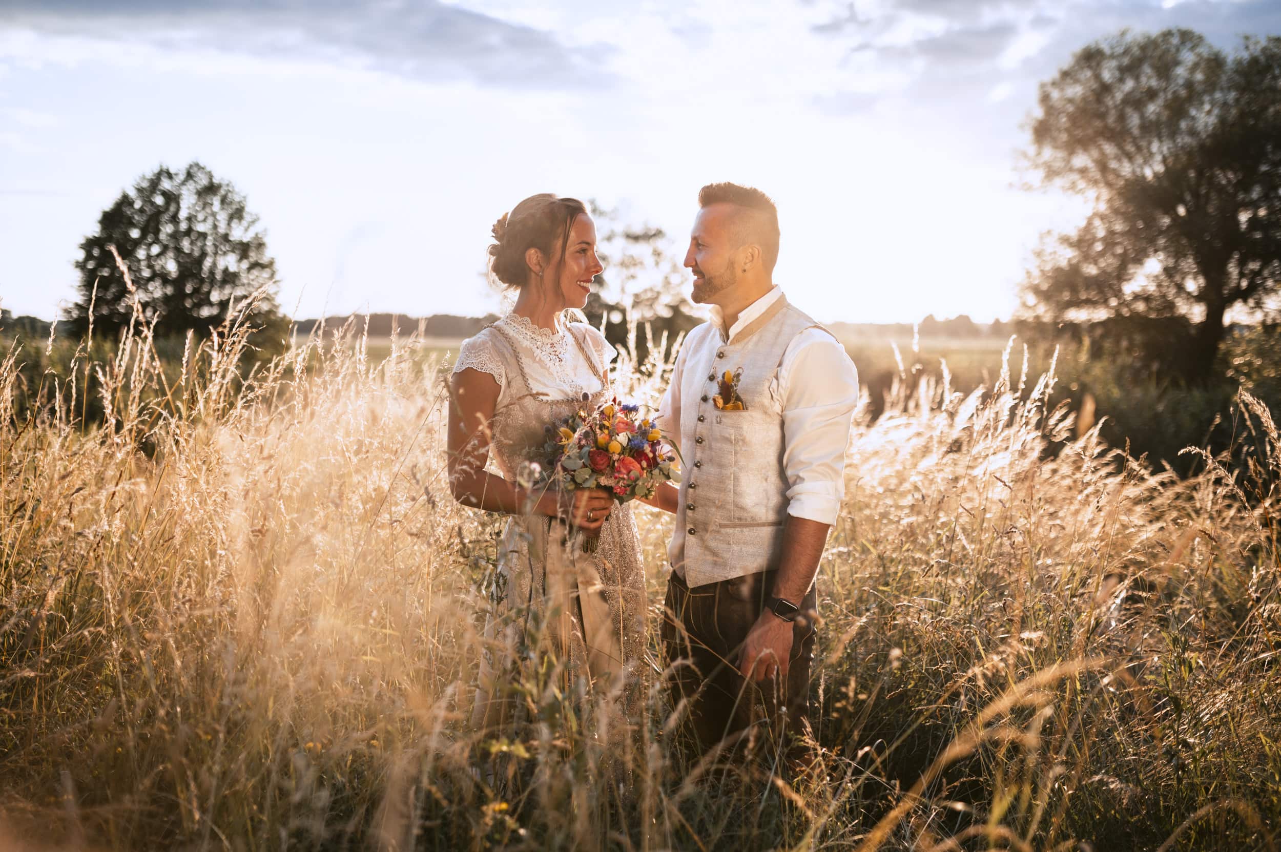 Brautpaar beim Hochzeitshooting in einem Feld mit hohem Gras beim Sonnenuntergang
