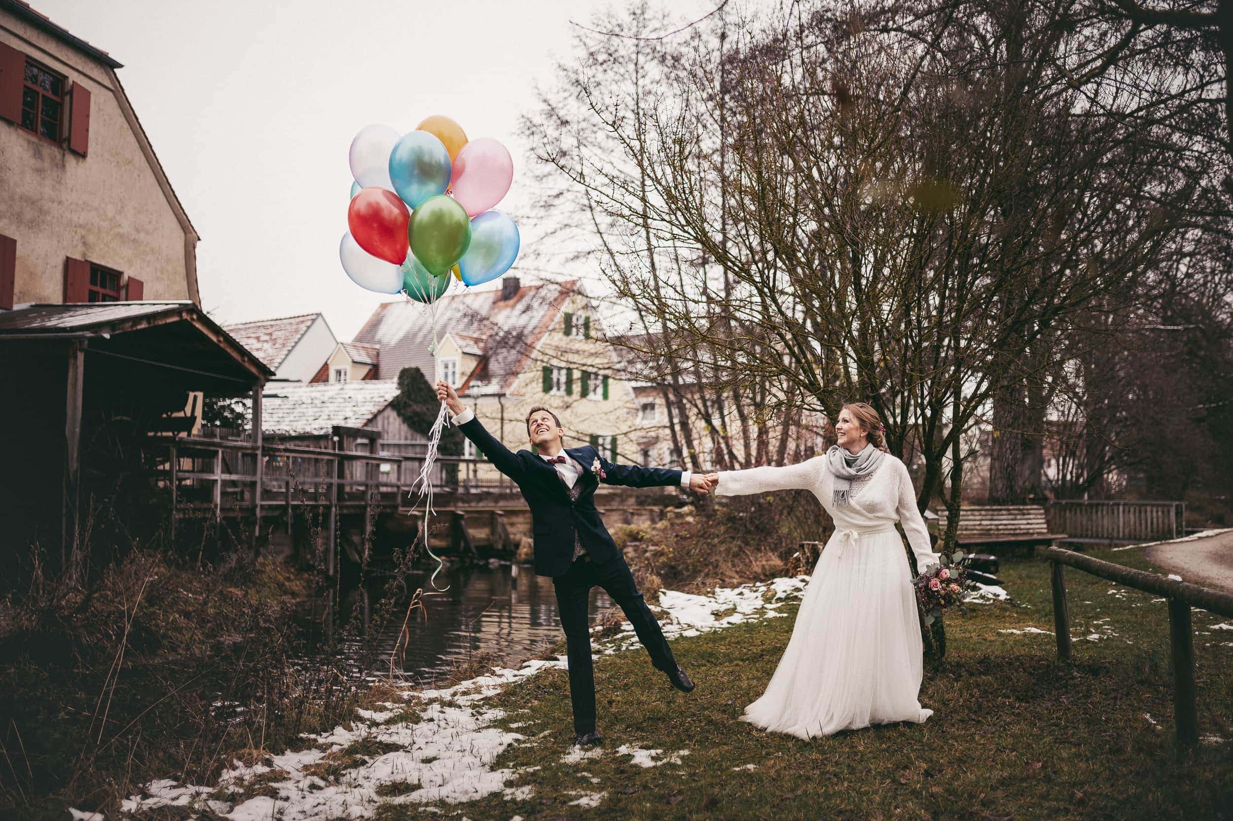 Bräutigam hält Luftballons und seine Braut hält ihn fest, damit er nicht davon fliegt