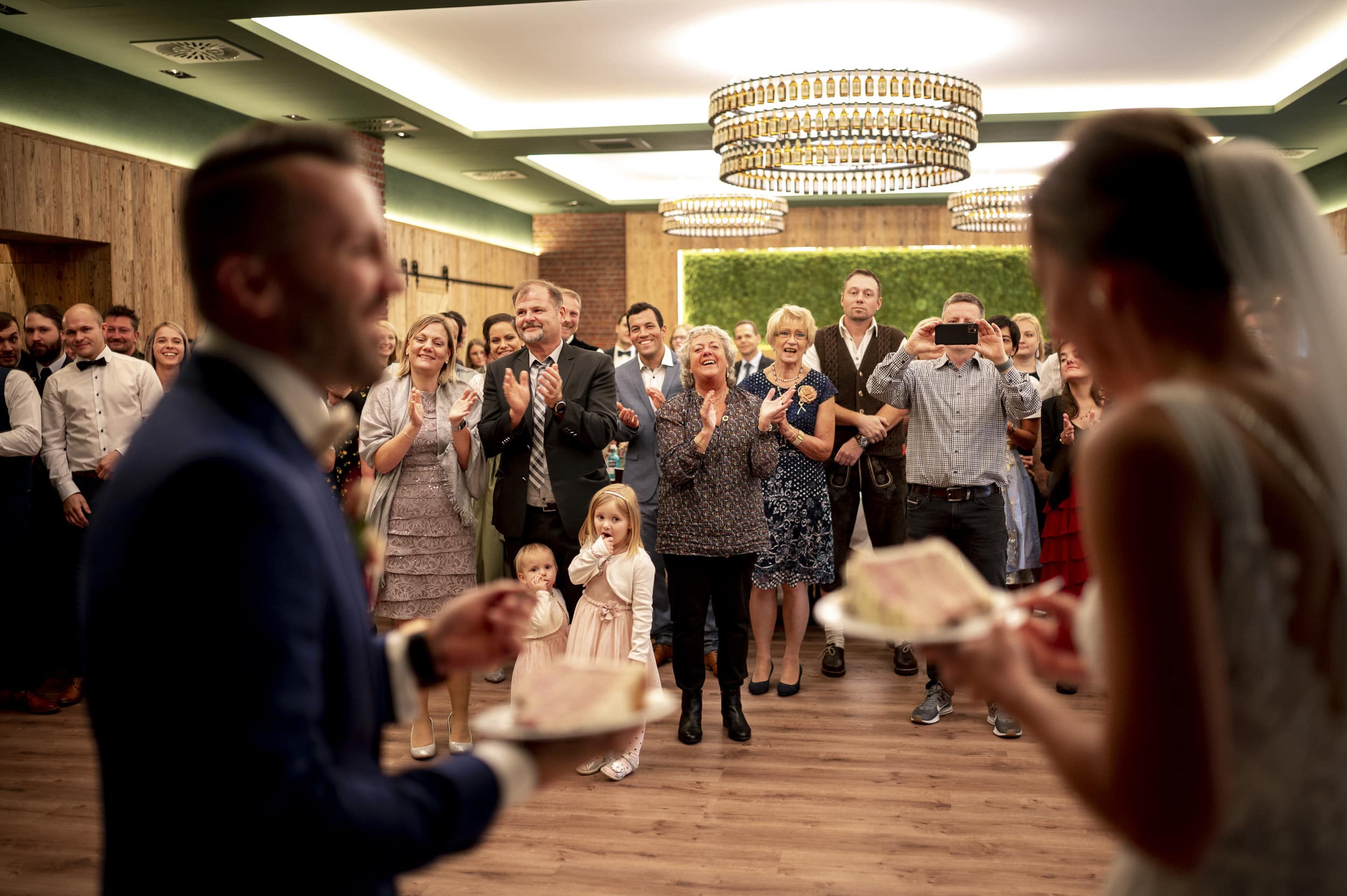 Brautpaar vor klatschenden Gästen nach angeschnittener Hochzeitstorte
