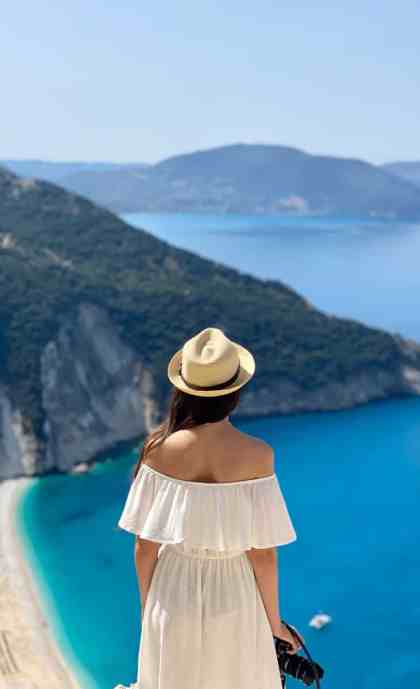 a woman in a white dress and hat looking at the ocean