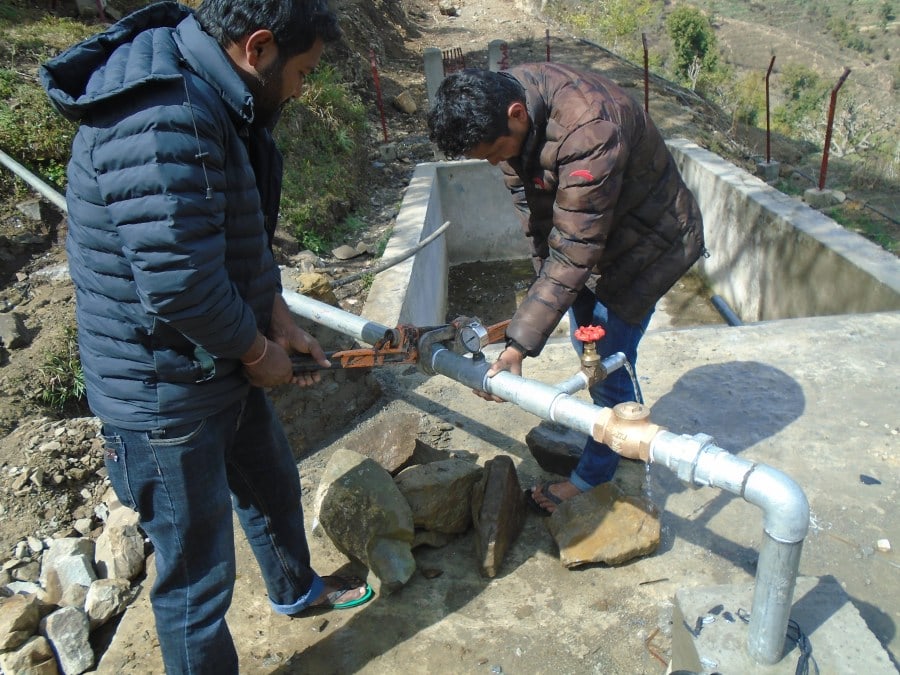 Two community members tighten the piping sections to ensure it is secure.