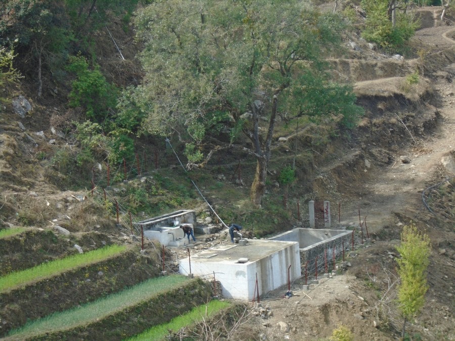 A wide shot of the length of the pipe as two community members work on the final touches.