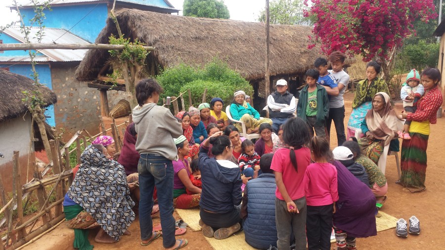 A community meeting taking place outside in front of houses in Magare