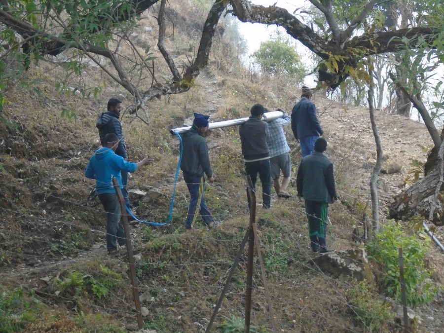 Three men carrying one the sections of the pipe to the top of the hill, as other community members help out. 