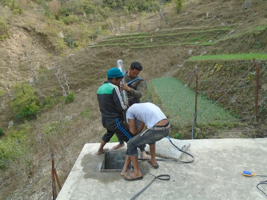 Three men install the solar-powered pump on a platform on a hill in the community.