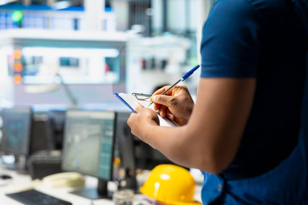 Inspection technician reviewing documents on a clipboard in an industrial setting.