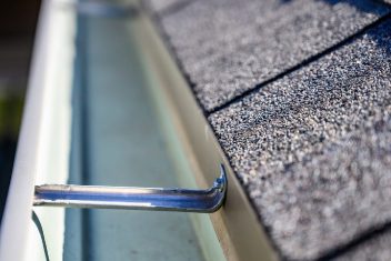 Close-up of a metal gutter on a shingled roof edge.