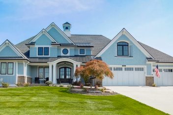 Large blue house with multiple gables, front yard, and attached garage under a clear sky.