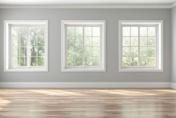 Empty room with three large windows and hardwood floor.