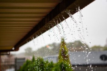 Rain droplets on window with blurred outdoor scene and cloudy sky.