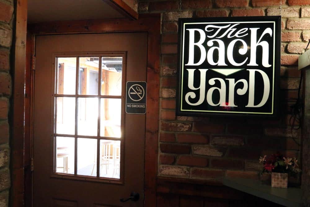 Sign for The Back Yard at Leroy's Classic Bar & Grill on brick wall.
