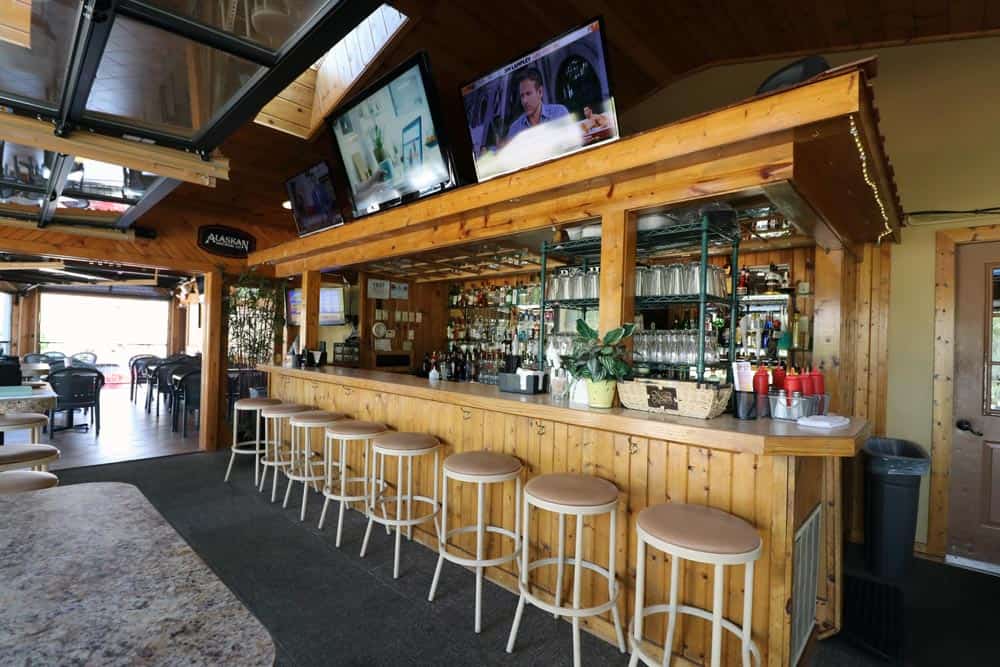 Bar area with wooden counter, bar stools, and multiple TV screens at Leroy's Classic Bar & Grill.