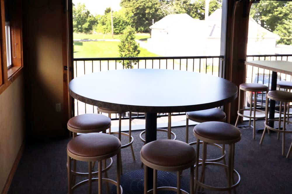 Round table with six stools on a balcony overlooking a green yard.
