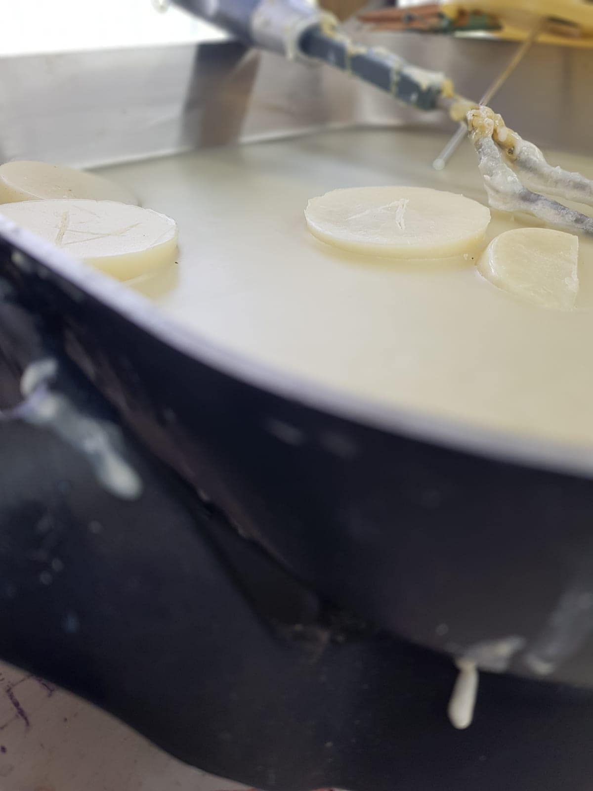 A dark pan containing circular slices of white wax floating in a clear liquid