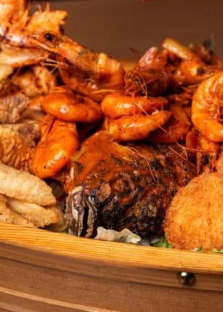 Seafood platter featuring shrimp, fish, and fried items on a wooden serving tray.