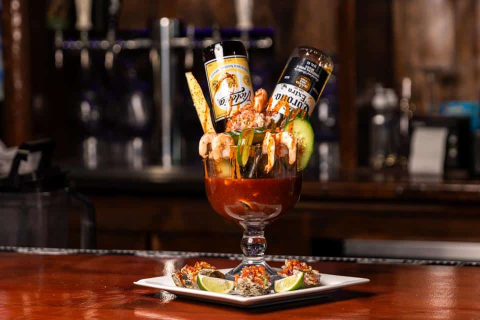 Decorative cocktail with beer bottles, lime, and fruit garnishes in a glass.