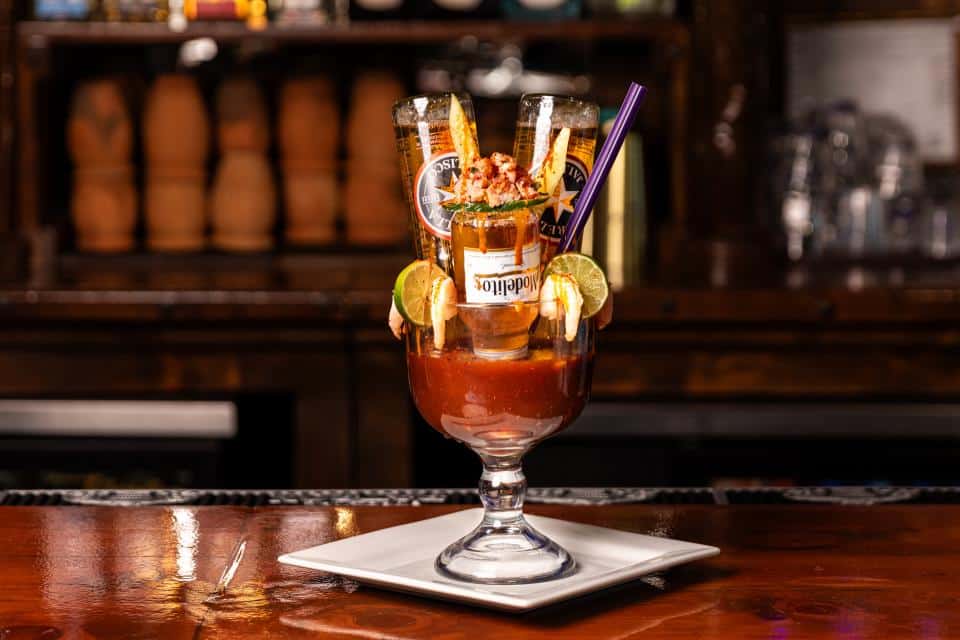 Colorful cocktail with beer bottles and garnishes on a bar counter.