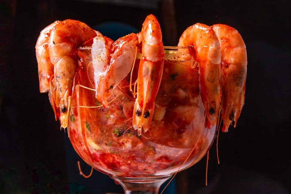Fresh shrimp arranged around a glass with seafood cocktail inside.