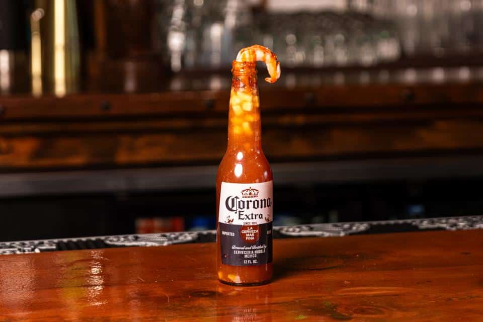 Unique beer bottle with a shrimp-shaped top on a wooden bar.