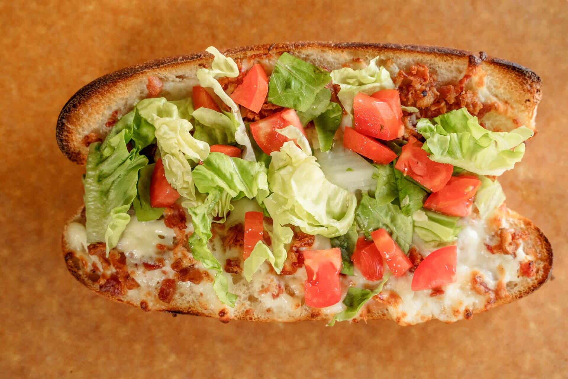 Close-up of a Sicilian pizza with lettuce and tomatoes on top.