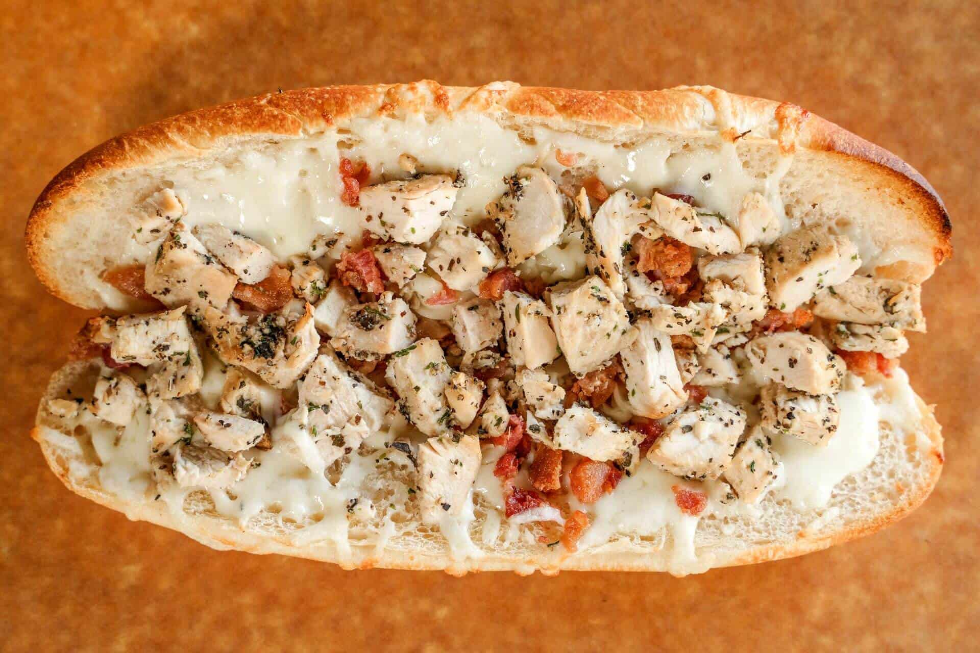 Close-up of Sicilian pizza with chicken, bacon, and cheese on a bread loaf.