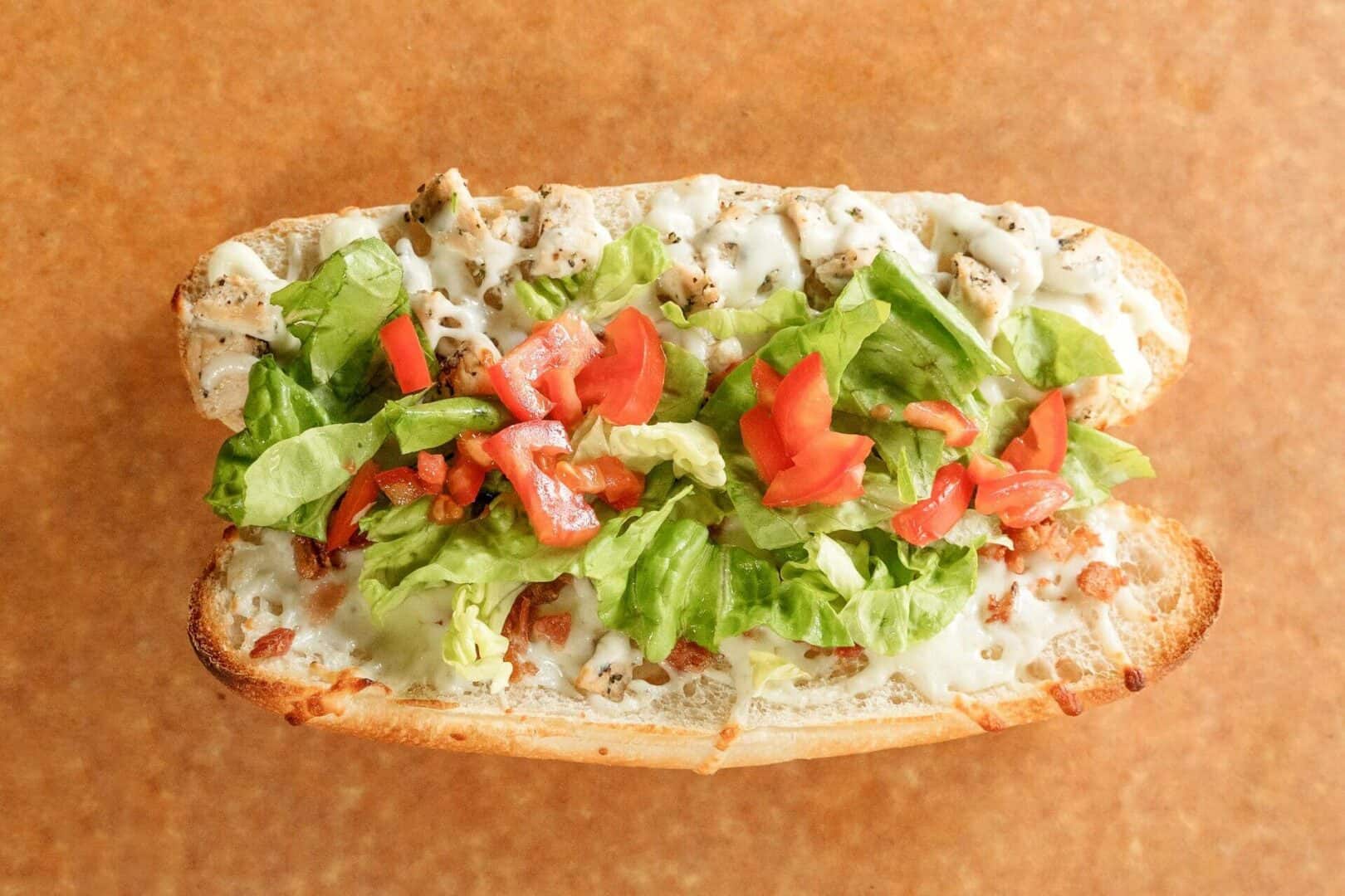 Fresh chicken sub with lettuce, tomato, and sauce on a bun.