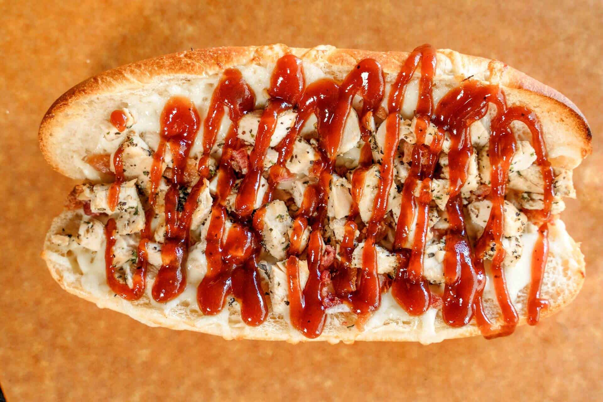 Close-up of BBQ chicken sub with sauce and toppings.