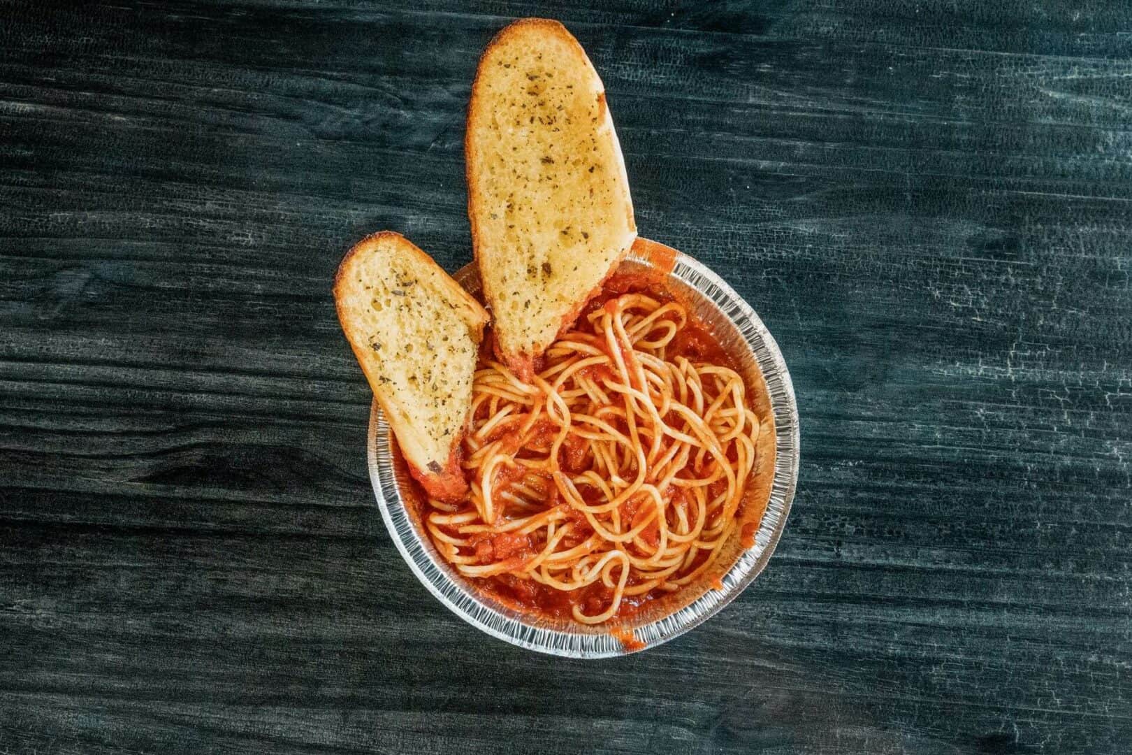 Spaghetti in tomato sauce with two garlic bread slices on a dark wooden table.