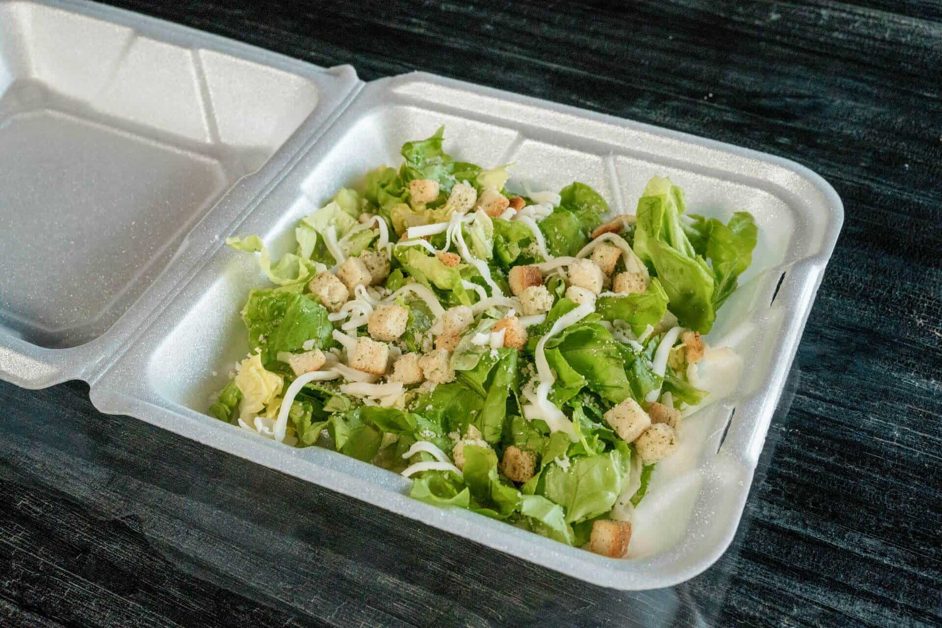 Fresh Caesar salad with lettuce, croutons, and cheese in a foam container.