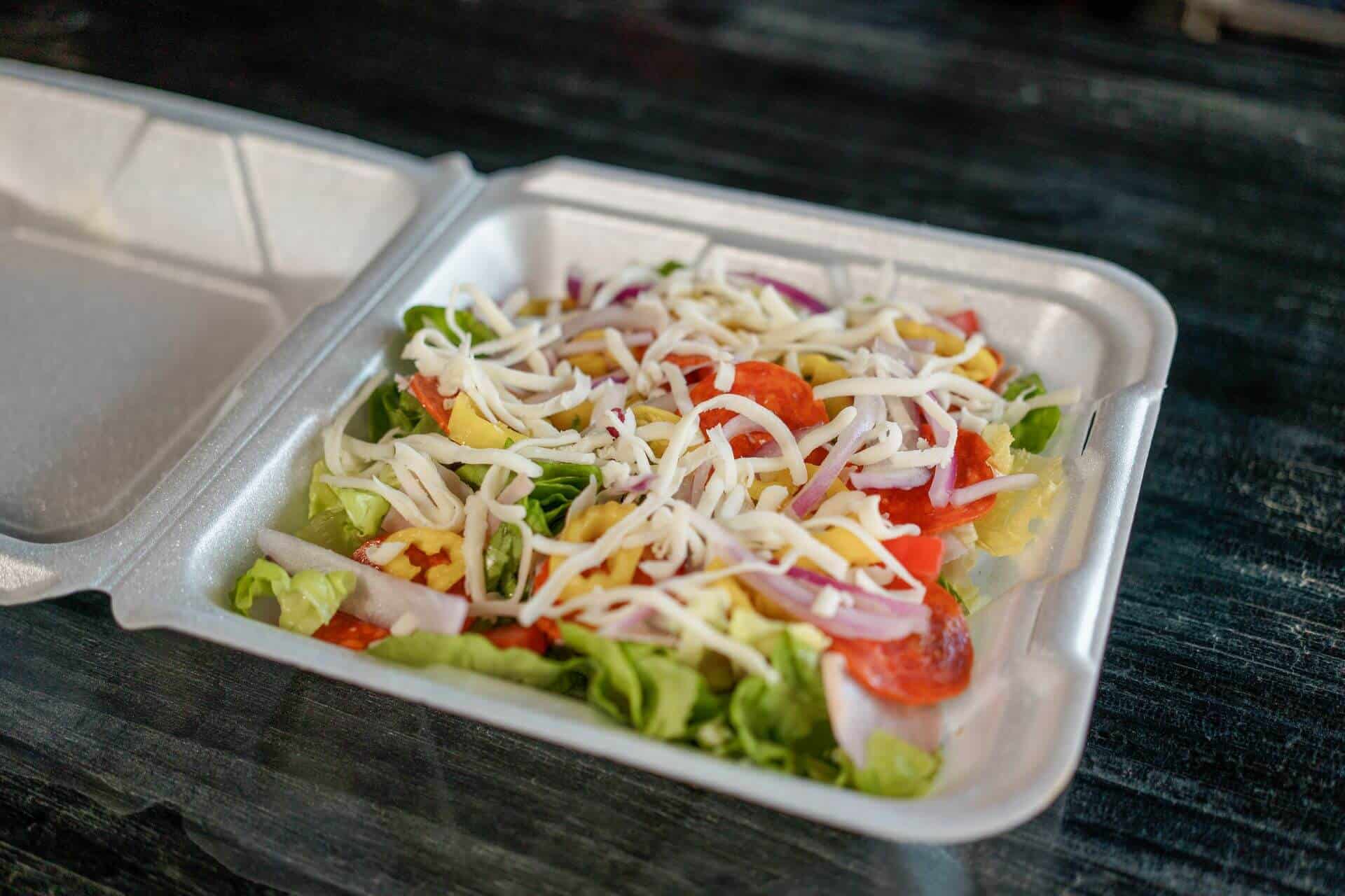 Fresh antipasto salad with lettuce, tomatoes, cheese, and onions in a takeout container.