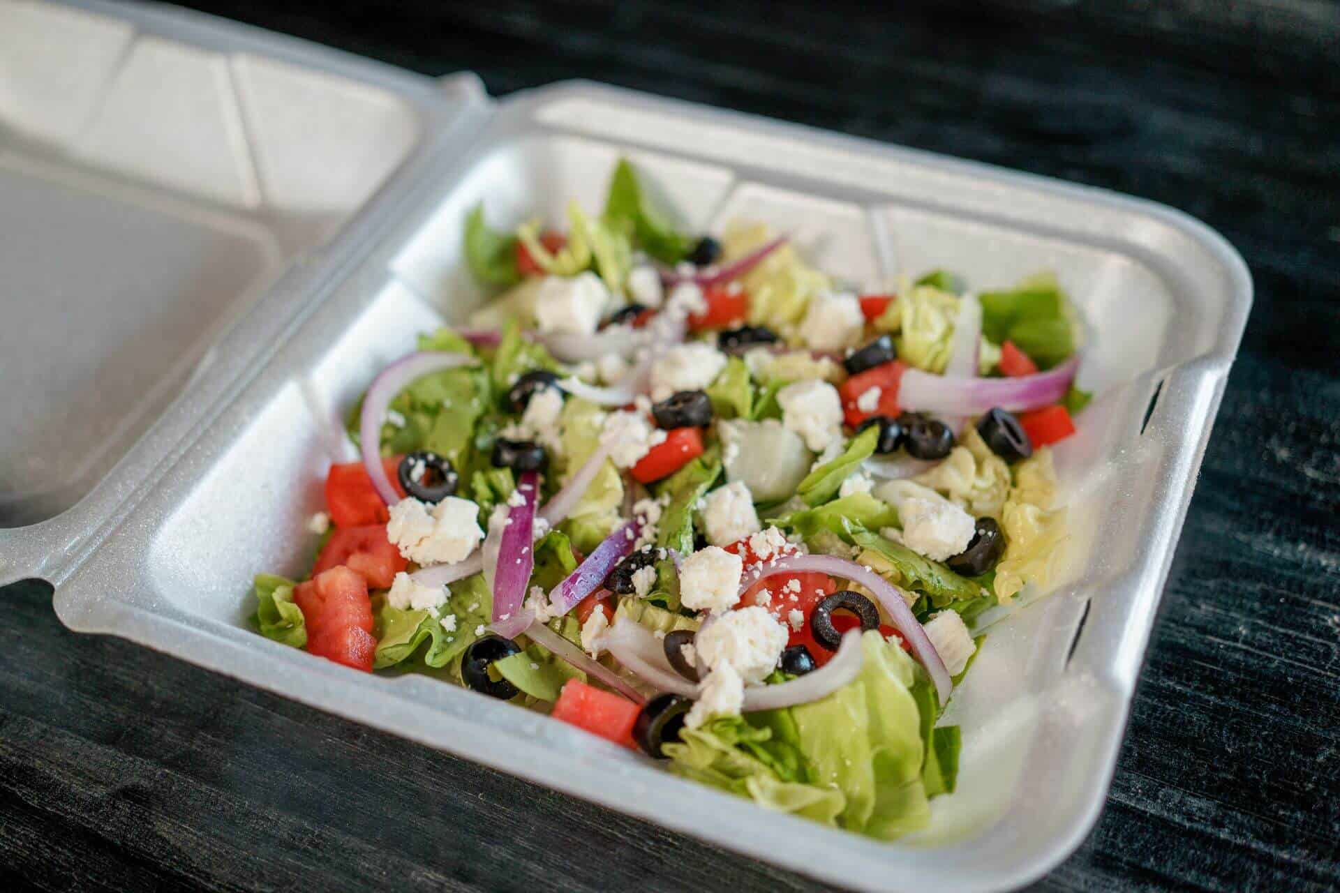 Fresh Greek salad with vegetables and feta cheese in takeout container.